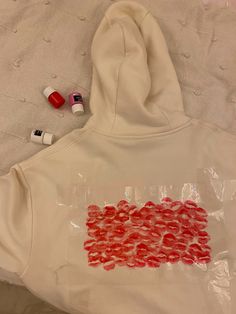 a white hoodie with red hearts painted on it and some other items next to it