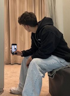 a young man sitting on top of a suitcase holding a cell phone in his hand