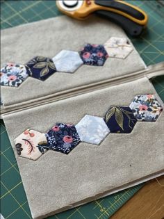 two pieces of fabric with flowers on them next to scissors and sewing needles, sitting on top of a cutting board