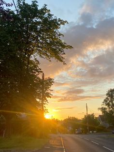 the sun is setting behind some trees on the side of the road with no cars