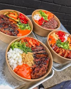 four bowls filled with meat and vegetables on top of a metal table next to a brick wall