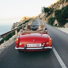 a woman in a red convertible driving down the road