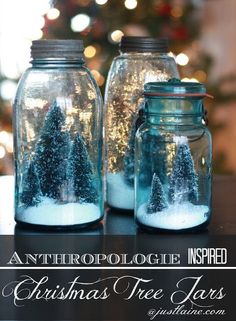 two glass jars filled with snow and trees on top of a table next to a christmas tree