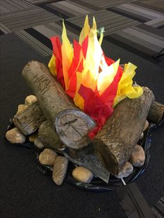 a fire pit made out of logs and colored paper on top of rocks with a knife next to it