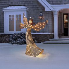 a lighted angel in front of a house with snow on the ground and lights around it