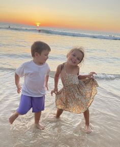 two young children playing in the ocean at sunset