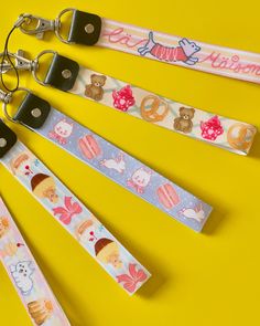 four keychains with different designs on them sitting next to each other in front of a yellow background