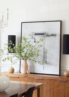 a vase with some flowers in it sitting on a table next to a large painting