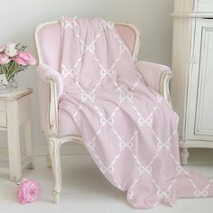 a pink blanket sitting on top of a white chair next to a vase with flowers