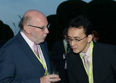 two men standing next to each other in suits and ties holding drinks at an event