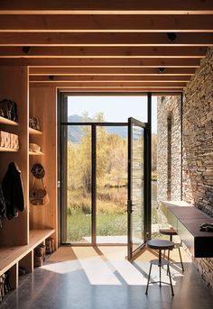 the inside of a house with open doors and stone walls, overlooking a grassy field