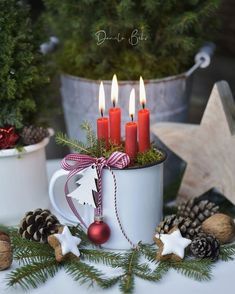 a cup filled with candles sitting on top of a table next to pine cones and christmas decorations