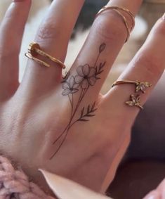 a woman's hand with three rings on it and flowers tattooed on the middle finger