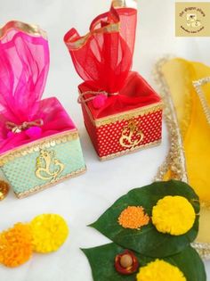 three small boxes with colorful ribbons and decorations on top of a white surface next to green leaves