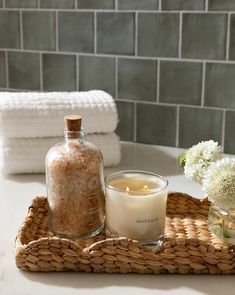 a candle sits on a tray next to some flowers and towels in a bathroom setting