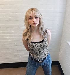 a woman standing in front of a white brick wall with her hands on her hips