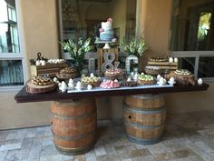 a table topped with cakes and desserts on top of wooden barrel tables next to windows