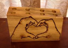 two hands making a heart shape with their fingers on a wooden block that is sitting on a table