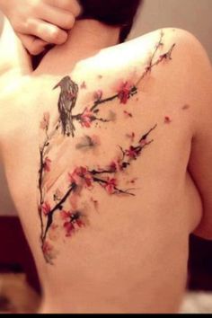 the back of a woman's body with flowers on it and a bird tattoo