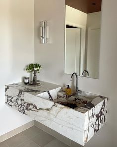 a bathroom sink with marble counter top next to a mirror and vase on the wall