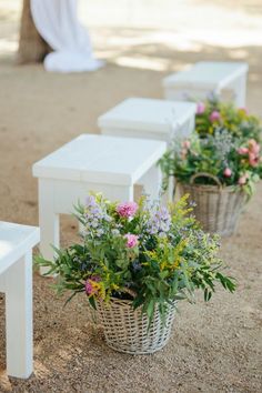 three white benches sitting next to each other with flowers in the baskets on top of them