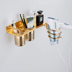 a gold shelf with cups, toothbrushes and hairdryer on it hanging from the wall