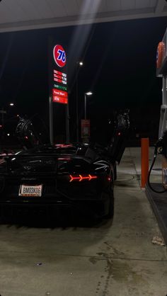 a black sports car is parked at a gas station with its hood open and lights on