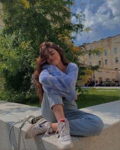 a young woman sitting on the edge of a cement wall with her hands behind her head