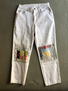 a pair of white jeans with colorful patches on the bottom and side, sitting on top of a bed