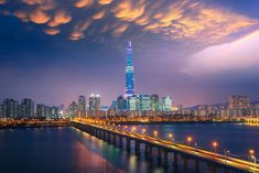 the city skyline is lit up at night, with clouds in the sky above it