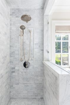 a walk in shower sitting next to a window with white tile on the walls and floor