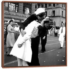 a man and woman kissing on the street while people watch from the side walk behind them