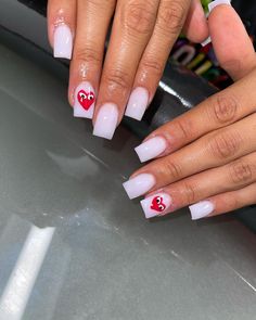 two hands with white and red nail polish holding each other's fingers while they both have hearts painted on them