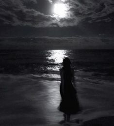 a woman standing on top of a beach next to the ocean under a full moon