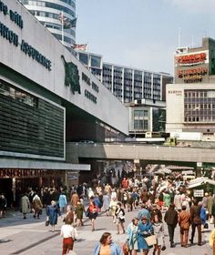 a crowd of people walking down a street next to tall buildings in a city center