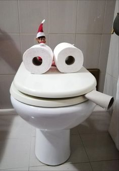 a toilet with two rolls of toilet paper on it's lid and an elf hat