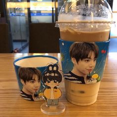 two coffee cups sitting on top of a wooden table next to an iced drink in a plastic cup