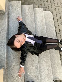 a woman in black jacket and tie laying on steps with her hand up to the side