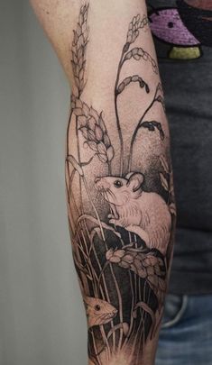 a person with a tattoo on their arm holding a mouse in the grass and flowers