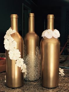 three gold vases with white flowers are sitting on a countertop next to each other