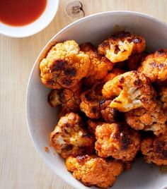 a white bowl filled with cauliflower next to a cup of tea and sauce