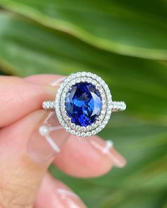 a woman's hand holding a ring with a blue stone in the center and diamonds around it