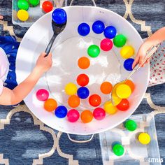 two children are playing with colorful balls in a white bowl on a blue tablecloth