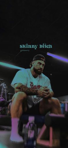 a man sitting on top of a bench in front of a wall with the words skinnyy bitten