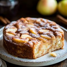 a cake sitting on top of a white plate covered in powdered sugar next to apples