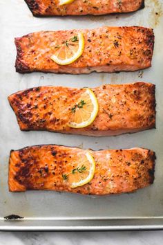 three salmon fillets on a baking sheet with lemon slices