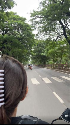 a woman driving down the road with her hair comb in her hand and trees lining the street behind her