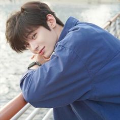 a young man leaning on a railing next to the water with his hand under his chin