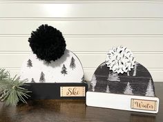 two winter hats sitting on top of a wooden table next to a pine tree and sign