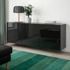 a black sideboard with a potted plant on top and green rug in front